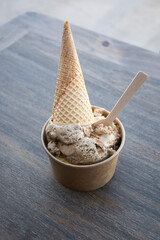 delicious pot of artisanal dulce leche ice cream with cone on wooden table on sunny day top view