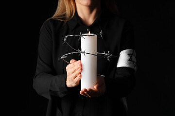 Mature woman with candle and barbed wire on black background, closeup. International Holocaust...