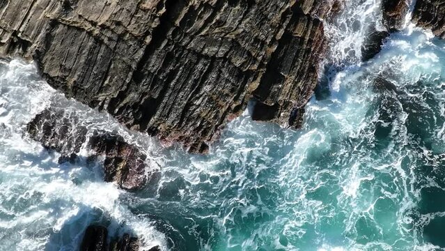 Aerial footage of turquoise ocean waters washing rugged, rocky shoreline