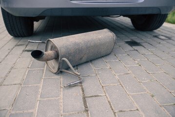 the rusty exhaust pipe, the car's muffler has fallen off and is lying on the road
