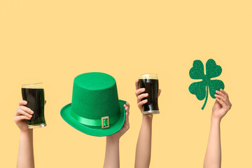 Hands with beer, clover and leprechaun's hat on yellow background. St. Patrick's Day celebration