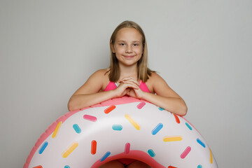 Obraz na płótnie Canvas Smiling child girl with pink rubber inflatable ring swimming pool float standing on white studio wall background