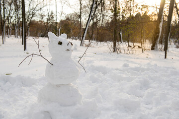   Funny snowy figure of a snowman with the face of a cat or other animal in a snowy park. Fun winter activities.