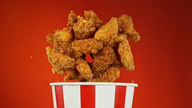 Super Slow Motion of Exploding Fried Chicken Pieces from Bucket. Isolated on Red Background. Studio Shot of Flying Food. Filmed on High Speed Cinema Camera, 1000fps.