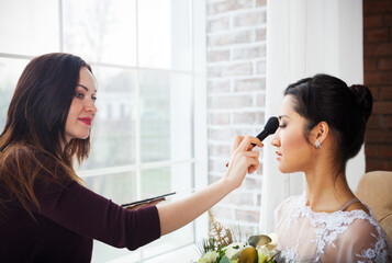 Make-up artist doing make up for young beautiful bride