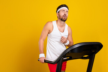 Portrait of tired handsome guy intense dynamic run treadmill empty space isolated on yellow color background