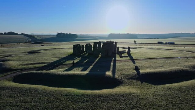 Drone shot pulling back from backlit Stonehenge and low sun with long shadows