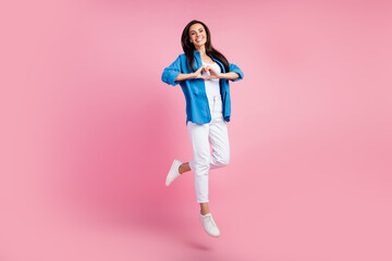 Full size photo of candid sincere girl dressed blue shirt white trousers jumping show heart symbol isolated on pink color background