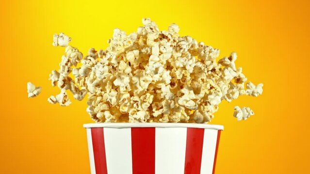Super Slow Motion of Exploding popcorn from Bucket. Isolated on Golden Background. Studio Shot of Flying Food. Filmed on High Speed Cinema Camera, 1000fps.