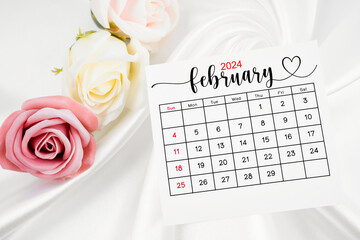 February 2024 calendar page and rose flower on white satin textile.