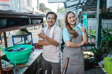 indonesian couple standing behind traditional food cart with thumb up gesture