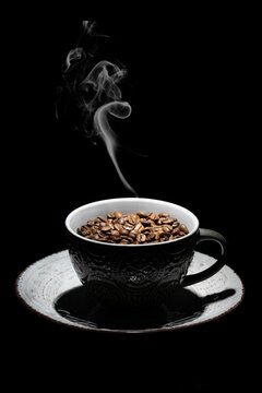 Rostade kaffebönor i en keramisk kopp på en svart bakgrund