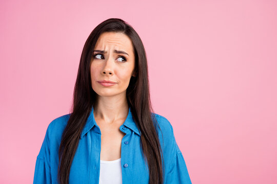 Photo of gloomy confused girl with straight hairdo dressed blue shirt look at proposition empty space isolated on pink color background