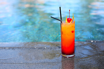 Glass with a bright tequila sunrise cocktail by the pool.