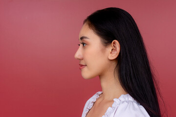 Side view of a young Asian woman with a serene expression, isolated on a striking red background.