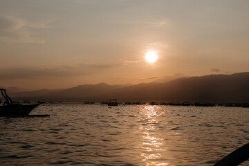 Warm peach sunrise over the island and mountains view from the ocean. Early morning on the trip. Fishing boats return to shore