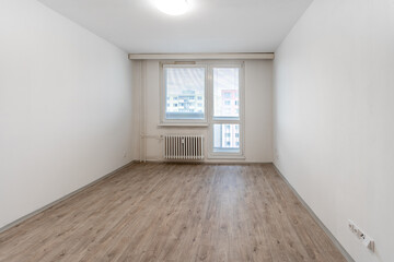 empty room with white walls, a large window providing natural light, a radiator beneath it, and a wooden floor, presenting a blank canvas for potential home decoration or real estate showcasing