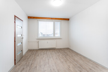 bare room with pristine white walls, a wooden laminated floor, and a large window that allows...