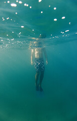Body of a Man underwater with sunlight shining down on him. clear blue water with bubbles. Surreal scene. Creative