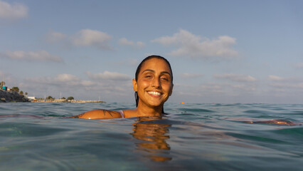 latin tattoo woman in the ocean in summer under sunset light on a tropical sea with a big and energetic smile.