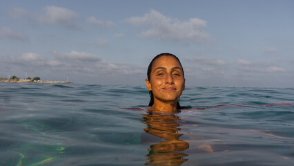 latin woman in the ocean in summer under sunset light on a tropical sea smiling