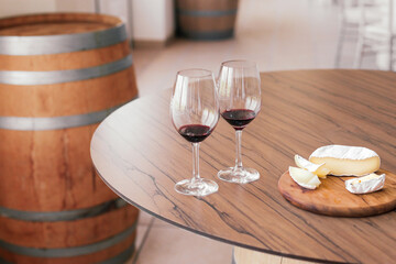 Two glasses of wine with cheese snacks on a wooden table, wine barrel on the background 