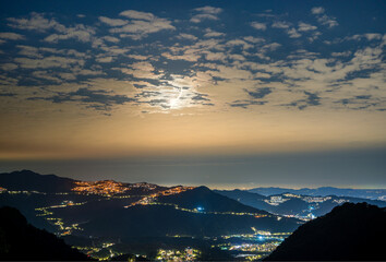 Stunning views of the full moon illuminate the tranquil landscape of the mountains, highlighting the city lights amid natural beauty. New Taipei.