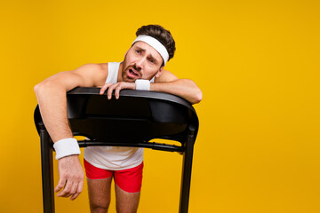 Portrait of exhausted weak young man struggling running treadmill empty space isolated on yellow...