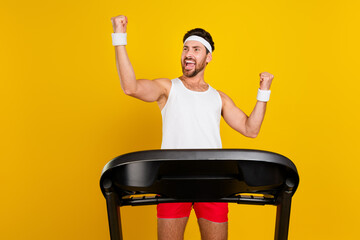 Photo of good mood lucky guy activewear walking treadmill rising fists empty space isolated yellow...