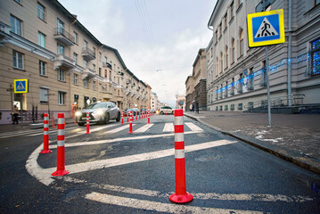 Pedestrian crossing sign and orange pole installed on crosswalk, road markings on zebra crossing. Traffic bollards on roadside, prevent parking car near pedestrian crossing. Selective focus