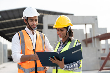 Asian male and female civil engineers wearing vest and helmet safety discussing on document at...