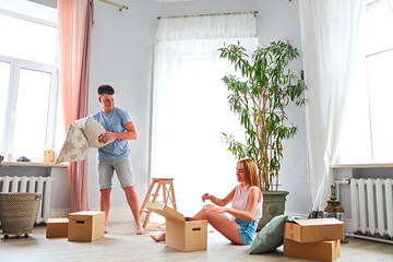 Young happy couple in room with moving boxes - obrazy, fototapety, plakaty