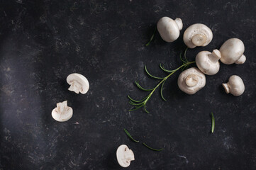 Champignon mushrooms on a dark background with rosemary herbs, top view, natural light