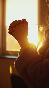 close-up of female hands palm to palm. the girl prays in front of the window at sunset. vertical video