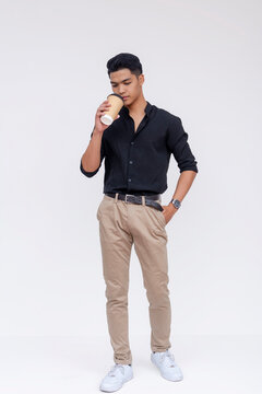 A fashionable young Filipino man enjoys a takeaway coffee cup, exuding an urban casual style on a white backdrop.