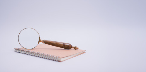 magnifying glass and spiral notebook on white table background