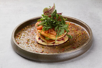 Beautiful pancakes with salmon, arugula on a white plate on a grey background.