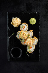 Salmon tempura roll top view on a textured black slate with condiments