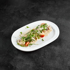 A sumptuous creamy seafood platter enhanced with fresh greens and cherry tomatoes, served on a pristine white oval plate from a top-down perspective