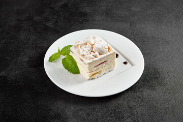 Delicate meringue cake with creamy cheese filling, garnished with a sprig of mint on a white plate