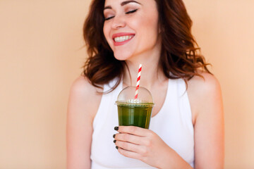 Delighted female with green smoothie laughing against wall background