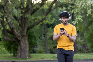 Fit indian sportsman with headphones checks phone in park setting