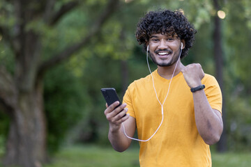 Cheerful young indian man enjoying music on smartphone during outdoor workout