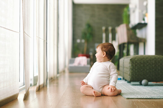  Portrait of adorable baby sitting on the floor in living room, looking to the side