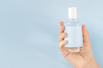 female hand holding a bottle of perfume with a blue label on a blue background, space for your text.