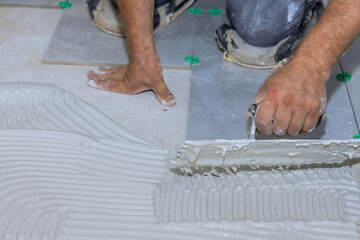 Tiler applies adhesive mortar cement plaster to floor in preparation for installation of ceramic...
