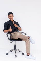 A relaxed young Filipino man in casual office attire sitting on an office chair and giving a thumbs up against a white background.