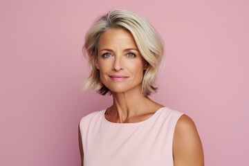 Beautiful middle aged woman looking at camera and smiling while standing against pink background