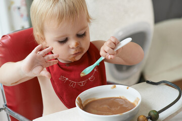 High chair, eating and baby with spoon in a house for nutrition, diet and fun while playing. Food,...