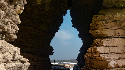 Woman standing in front of cave entrance and staring out to sea